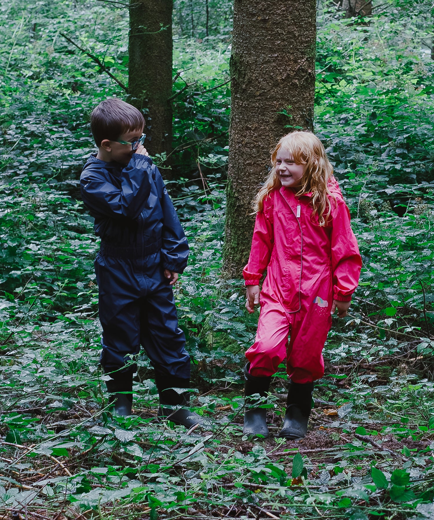 A young boy and girl wearing full length wet suits and Cotswold wellingtons in a wet woodland 