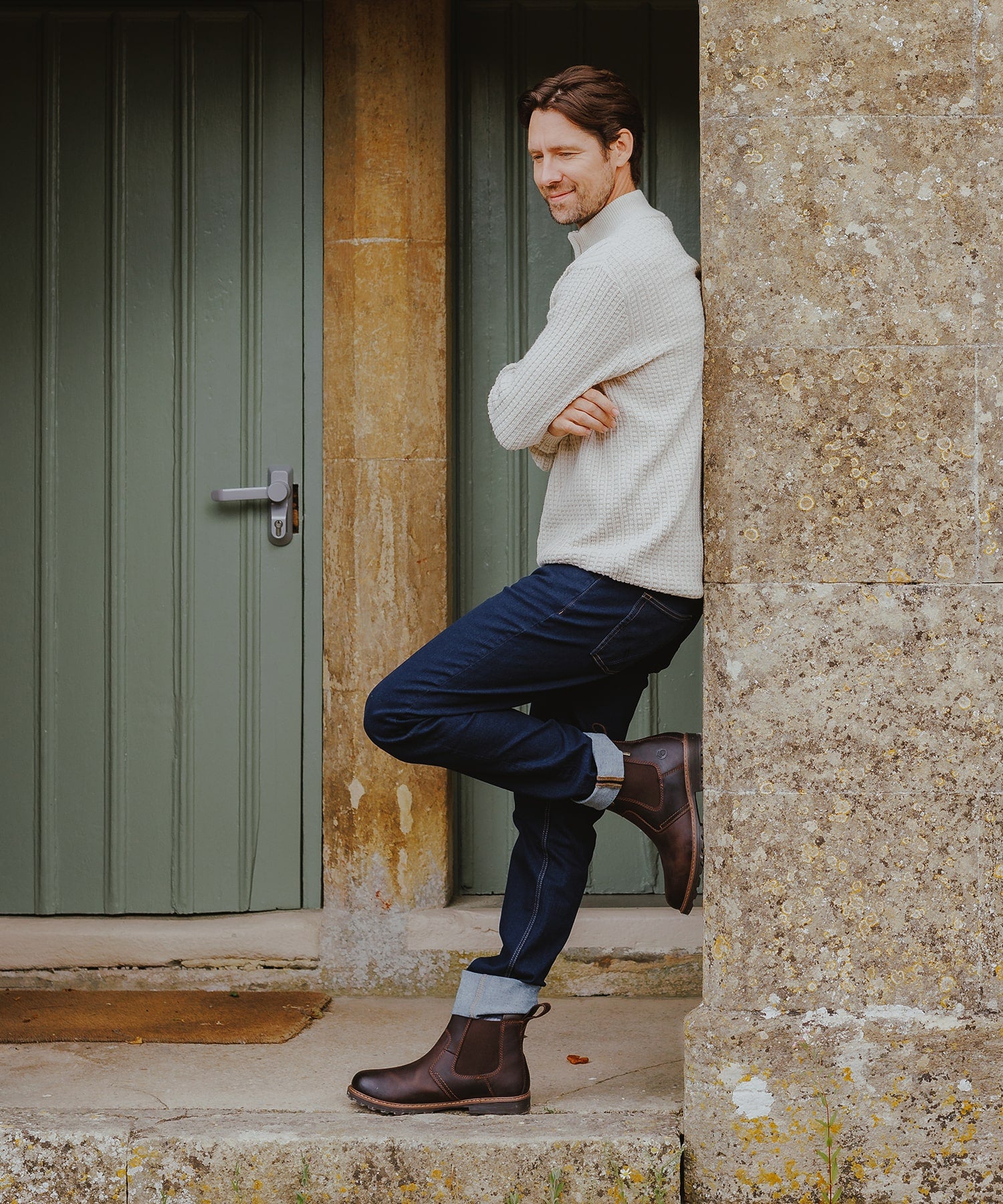 Man leaning against a wall in a porch, wearing a pair of Cotswold Dealer boots